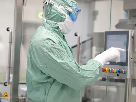 Eine Person in voller Schutzkleidung bedient ein Touchscreen-Bedienfeld in einer sterilen Labor- oder Produktionsumgebung.
